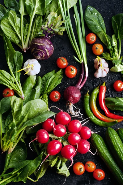 Fresh juicy vegetables and greenery, such as radish, onions, tomatoes, spinach, hot pepper, garlic, cabbage, kohlrabi, and radishes on a black surface. Vegetable background. Vegan concept