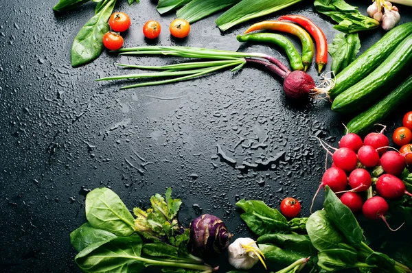 Fresh juicy vegetables and greenery, such as onions, tomatoes, spinach, hot pepper, garlic, cabbage, kohlrabi, and radishes on a black surface. Vegetable background. Vegan concept. Space for text