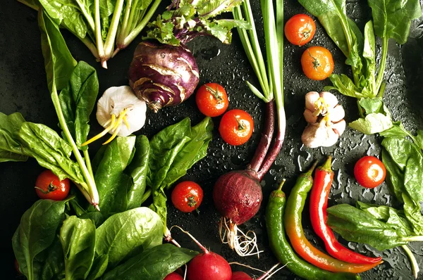 Fresh juicy vegetables and herbs, such as onions, tomatoes, spinach, hot pepper, garlic, cabbage, kohlrabi, and radishes on a black surface. Vegetable background. Vegan concept