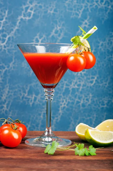Tomato juice in a glass on a wooden board. Blue background. Vegetarian concept. Non-alcoholic cocktail of tomato juice