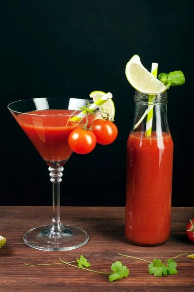 Tomato juice in a glass and bottle on a wooden board. Black background. Vegetarian concept. Non-alcoholic cocktail of tomato juice