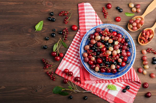 Blue plate with berries such as cherries, gooseberries, red and black currants, strawberries on a brown wooden background. Vegan concept. Berry diet. Berry background (wallpaper)