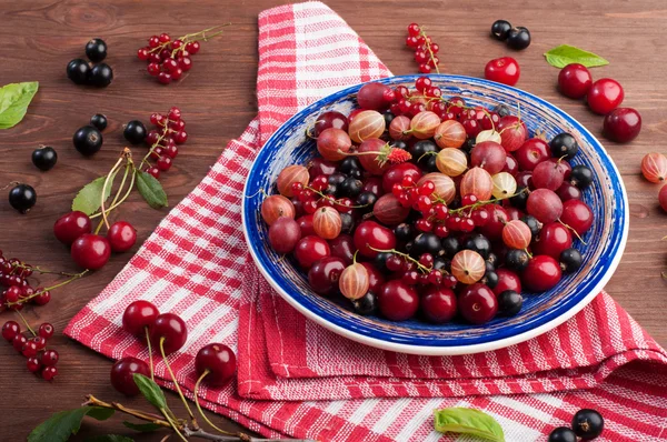 Blue plate with fresh juicy berries such as cherries, gooseberries, strawberries, black and red currants. Concept diet food. Summer berry background (wallpaper)