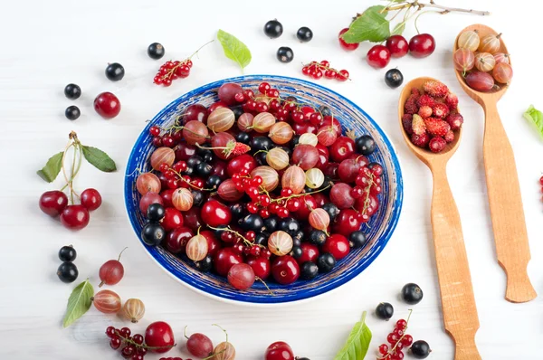 Blue plate with fresh juicy berries such as cherries, gooseberries, strawberries, black and red currants on a white wooden surface. Concept diet food. Summer berry background (wallpaper)