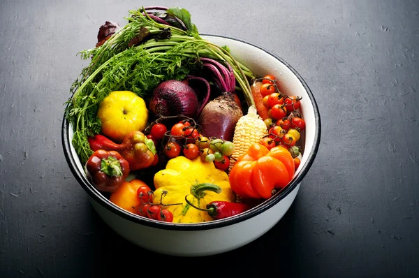Organic food concept. A bowl of fresh juicy colored vegetables on the dark surface. Bright peppers, cherry tomatoes, squash, onions, carrots and beets. Vegetarian, vegan products. Vegetable wallpaper