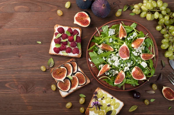Light summer salad with arugula, figs and blue cheese. Near fruit sandwiches with soft cheese and various toppings, such as figs, raspberries, green grapes and basil leaves. Low-calorie nutritious ready-made meal. Autumn menu