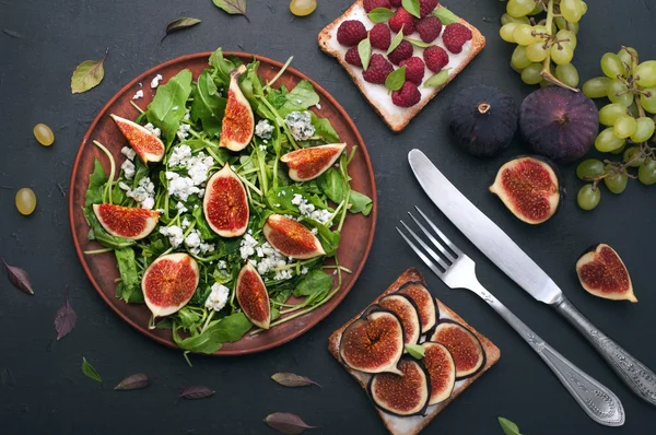 Light summer salad with arugula, figs and blue cheese. Near fruit sandwiches with soft cheese and various toppings, such as figs, green grapes and basil leaves. Low-calorie nutritious ready-made meal. Autumn menu