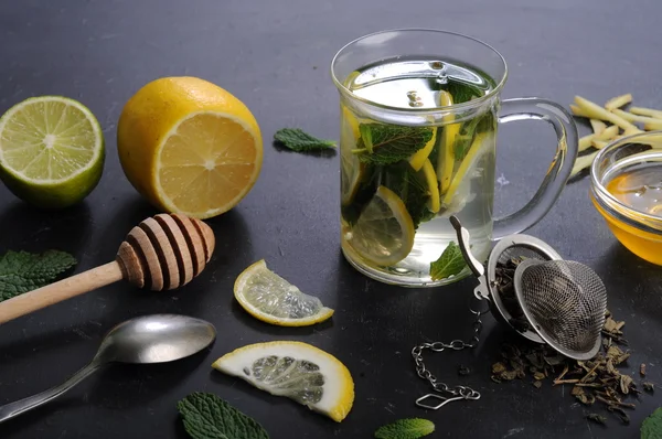 Tea with mint, lime, lemon and ginger on a dark background. Beside the ingredients for tea, such as chopped ginger root, peppermint leaves, slices of lemon and lime. The concept of treatment of colds, without the use of pills and medicines