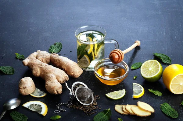 Ginger tea with lemon, lime and mint on black background. Beside the ingredients for tea, the same as the mint leaves, chopped ginger root, slices of lemon and lime. The concept of treatment of colds folk methods.