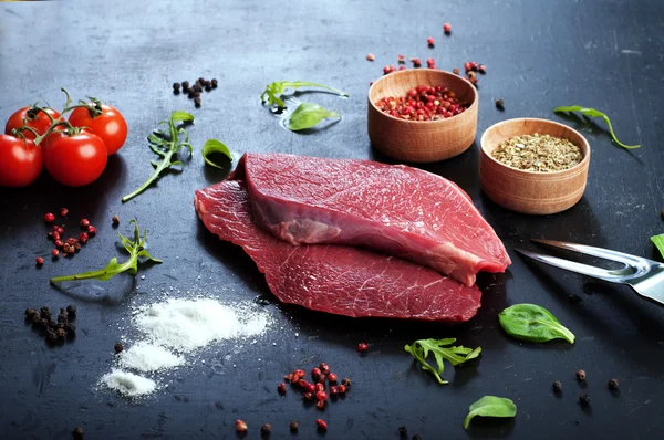 Raw beef steak on dark board. Backlight. The concept of preparing meat for cooking steaks