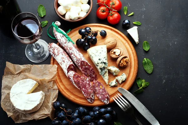 Italian food concept. Jerked sausage, various cheeses, blue grapes, vegetables and fruits on a dark background.