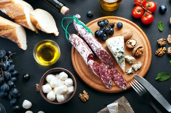 Italian food concept. Jerked sausage, various cheeses, blue grapes, vegetables and fruits on a dark background.