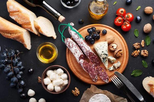 Italian food concept. Jerked sausage, various cheeses, blue grapes, vegetables and fruits on a dark background.