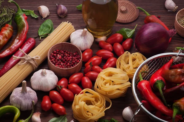 Italian food concept. Various ingredients for making pasta on a dark wooden surface. Pasta, tomato, garlic; hot pepper, seasonings and spices