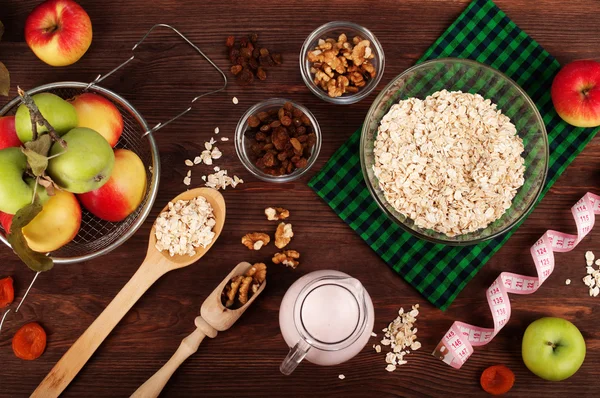Concept diet food. Oatmeal, dried fruits, apples and yogurt on a brown wooden background. Next measuring tape, which symbolizes the rapid decrease in volume of the body through proper diet.