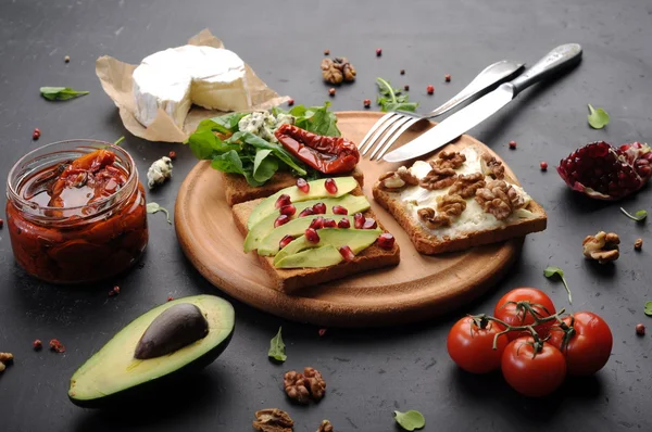 Sandwiches with a variety of toppings such as arugula, dried tomatoes, soft cheese, blue cheese, nuts and avocados on a dark background. The concept of healthy vegetarian food.