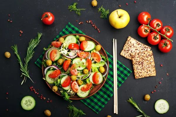 Concept diet food. Salad of fresh vegetables such as lettuce, purple onion, olives, cucumbers and tomatoes on a dark background. Vegetarian healthy dish