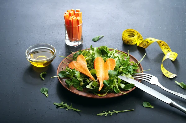 Concept diet food. Salad with arugula, leaf mash and carrots on a dark background. Vegetarian healthy dish that promotes weight loss.