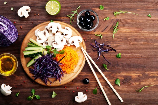 The concept of dietetic vegetarian food. Bright juicy shredded vegetables, such as carrots, purple cabbage, mushrooms and cucumbers, which lies on a circular wooden cutting board. Natural organic products, ready to eat