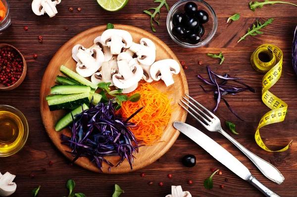 The concept of dietetic vegetarian food. Bright juicy shredded vegetables, such as carrots, purple cabbage, mushrooms and cucumbers, which lies on a circular wooden cutting board. Natural organic products, ready to eat