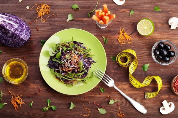 Concept diet food. Delicious vegetarian salad of arugula, leaf mash, purple cabbage and carrots on a brown wooden background. Natural organic healthy food, ready-to-eat