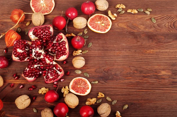 Bright background with juicy pomegranate, red dwarf apples, nuts and dried fruits on a brown wooden background. Place for writing text. It can be used as a substrate or a cover for the menu as a postcard or as an autumn background