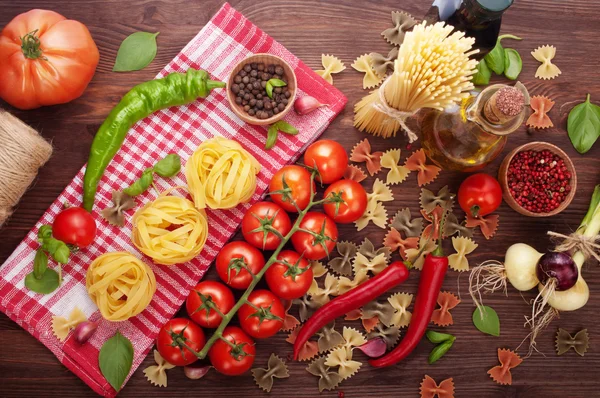 Italian food concept. Pasta and ingredients for making pasta on a brown wooden background. Pasta, chili pepper, cherry tomatoes, onions, olive oil, spices and seasonings on a wooden background.