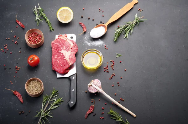 Raw beef steak, which lies on the cutting knife. Raw beef meat prepared for cooking steaks. Beside the ingredients for cooking steaks, spices and herbs.