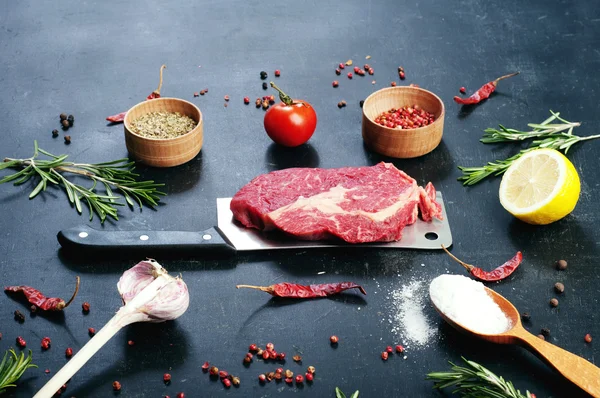 Raw beef steak, which lies on the cutting knife. Raw beef meat prepared for cooking steaks. Beside the ingredients for cooking steaks, spices and herbs.