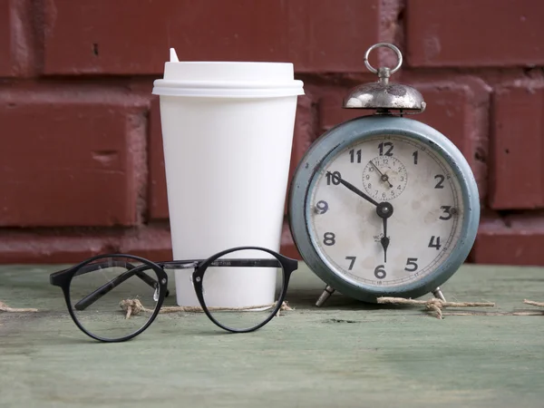 Cardboard cup hot coffee with old alarm clock and glasses