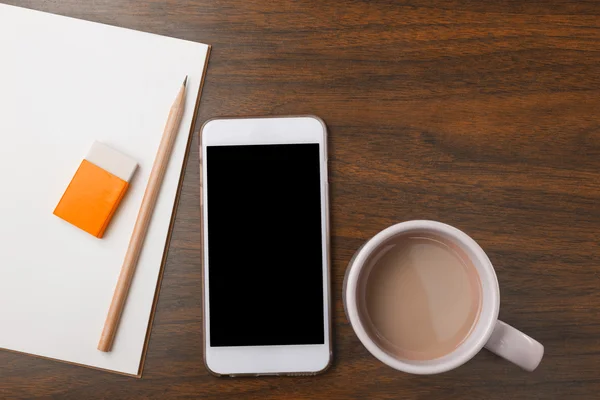Notebook, pencil, eraser, phone, and hot drink on wooden desk