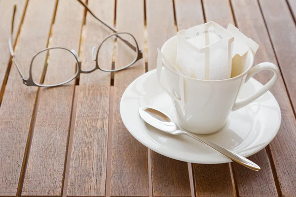 Coffee cup with packaged coffee on wooded table, blurred eyeglas