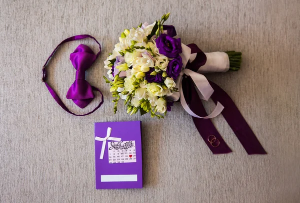 Bridal bouquet of white and blue flowers, rings, purple butterfly and invitation-cards lie on a light background