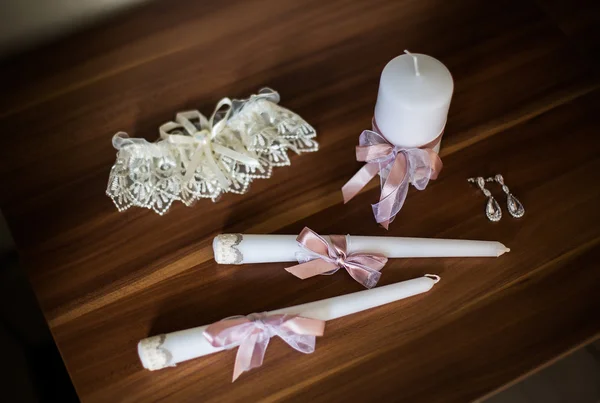 Earrings, beautiful candles and garter lying on a brown table, the morning of the bride