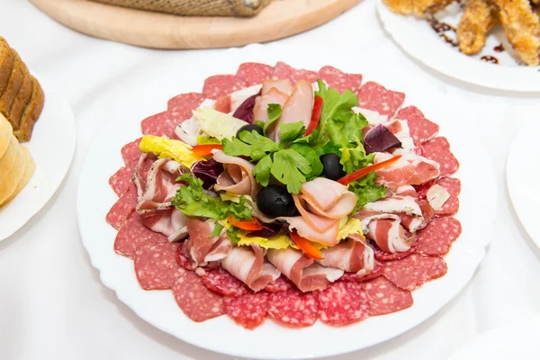 Plate of cold meats in the restaurant. Meat snacks. Smoked sausage and bacon, decorated with parsley and olives.