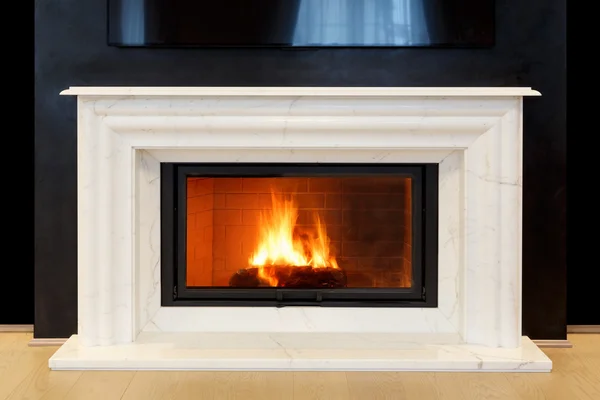 White, marble fireplace and burning fire.