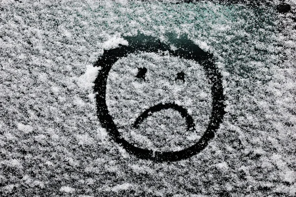 Sad smiley face drawn on snow-covered glass.