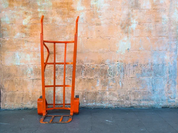 Red steel hand trolley or sack truck against orange brick wall