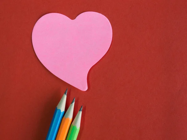 Pink heart-shaped memorandum on red paper with colorful pencils