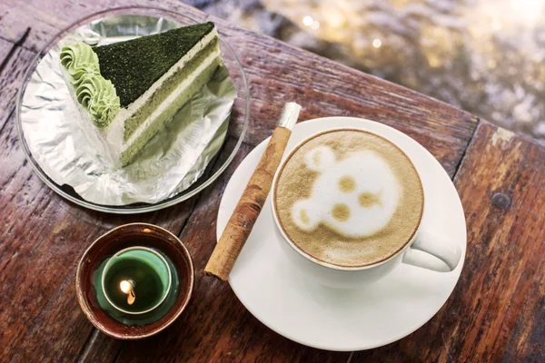 Cappuccino coffee with cinnamon stick and green tea cake on table with candle