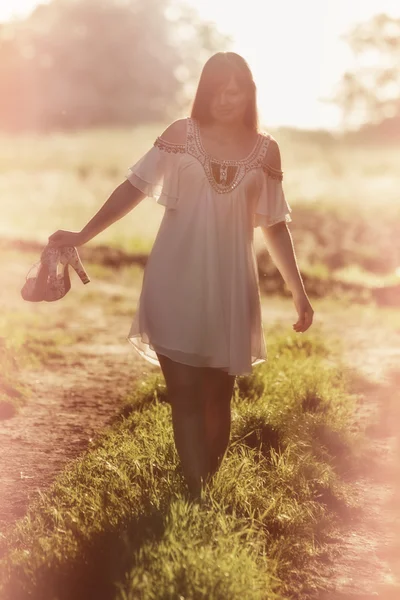 Young girl goes barefoot on a dirt road in a field at sunset. girl walking in a pine forest.