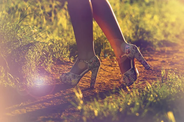 Young female legs walking towards the sunset on a dirt road.