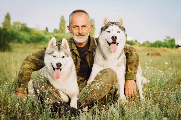 Old man with a beard sitting on a haystack with their dogs, enjoying summer sunset. Siberian Husky in the countryside.