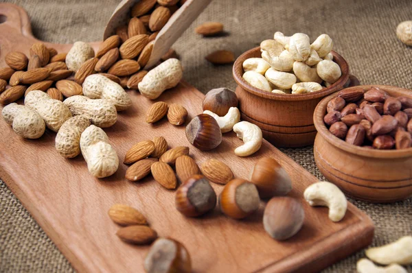 Almonds, cashew and hazelnuts in wooden bowls on wooden and burlap background