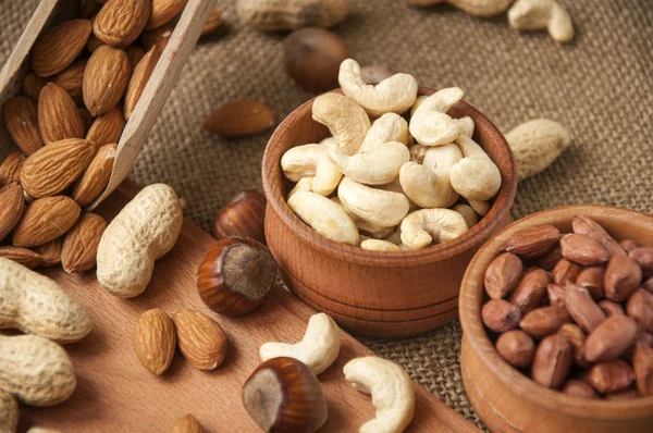 Almonds, cashew and hazelnuts in wooden bowls on wooden and burlap background