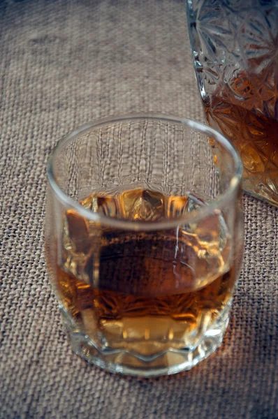Carafe and glass of whisky, whiskey bourbon on a burlap, sacks  background