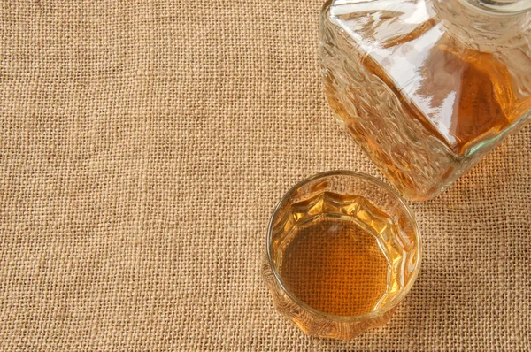 Carafe and glass of whisky, whiskey bourbon on a burlap, sacks  background