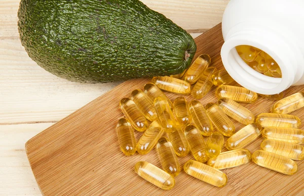 Cod liver oil omega 3 gel capsules isolated on wooden background with avocado