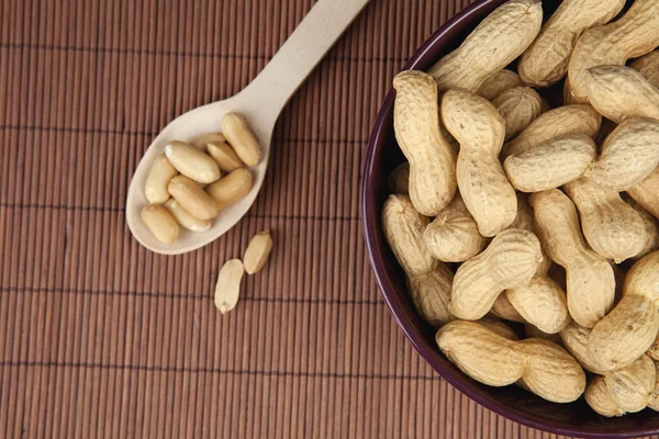 Peanuts on a brown wooden background in a ceramic bowl with spoon
