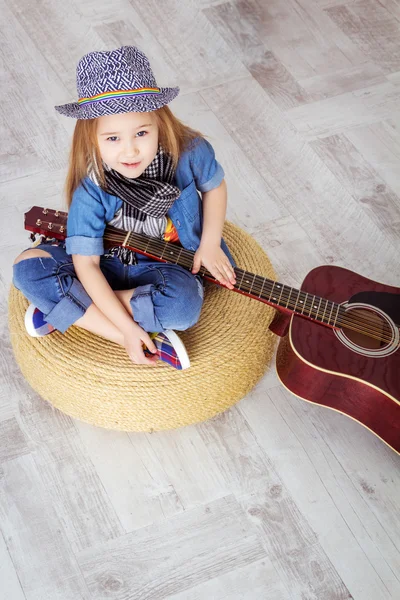 Little girl sitting in the lotus position and holding a guitar